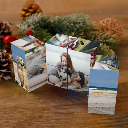 Three personalized photo cubes with images of a dog, a woman hugging a dog, a beach, and a baby meerkat, on a wooden surface with pinecones and festive decorations.