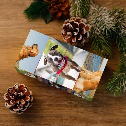 A wrapped gift on a wooden surface with a custom print featuring a collage of dog photos, flanked by pine cones and greenery.