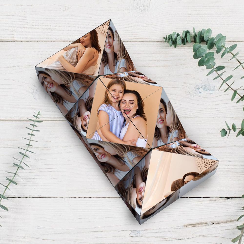 A 3D photo crystal cube displaying multiple images of a mother and daughter smiling together, set on a white wooden background with green leaves to the side.