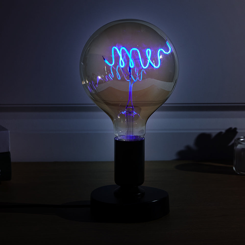 A plasma globe on a dark table with purple and blue electric arcs visible inside, casting a soft glow and subtle shadows on the surrounding area.