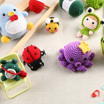 A collection of colorful crocheted amigurumi figures including animals and dolls, with balls of yarn and crochet hooks on a woven fabric surface.