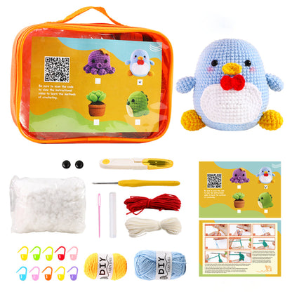 A DIY crochet kit with materials and instructions for creating a small blue and white penguin plush. Includes yarn, stuffing, tools, and a clear orange carrying case.