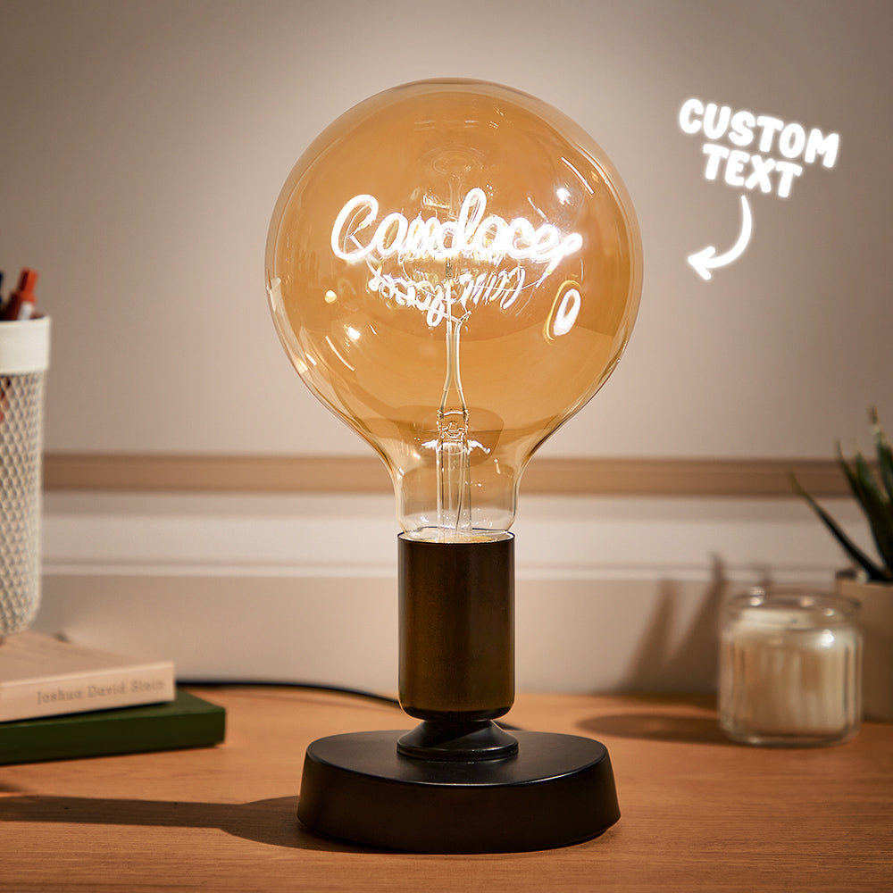 A large, glowing light bulb on a desk with custom text inside, indicating "Good day" in cursive neon script, next to a book and candle with "CUSTOM TEXT" mock-up arrow pointing towards the bulb.